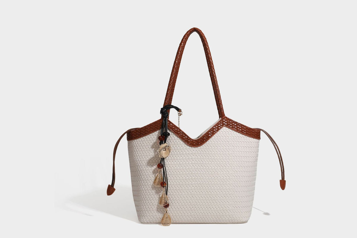Olivgrüne Tote-Bag in Korbgeflecht-Optik mit dunkelbraunen geflochtenen Schulterriemen, seitlichen Kordelzügen und Perlenanhänger in Goldoptik