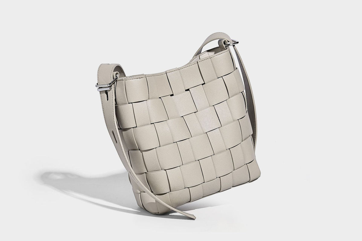 Hand-woven black-and-white checkerboard bucket bag with smooth black trim, silver-tone ring hardware, and adjustable