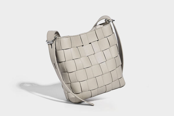 Hand-woven black-and-white checkerboard bucket bag with smooth black trim, silver-tone ring hardware, and adjustable