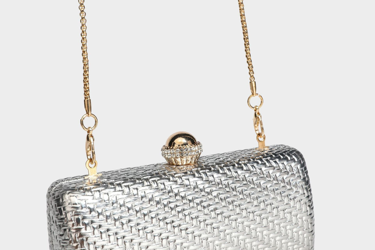 Small structured metallic woven-texture box clutch bag with jeweled kiss-lock dome clasp and slim gold chain strap, detail