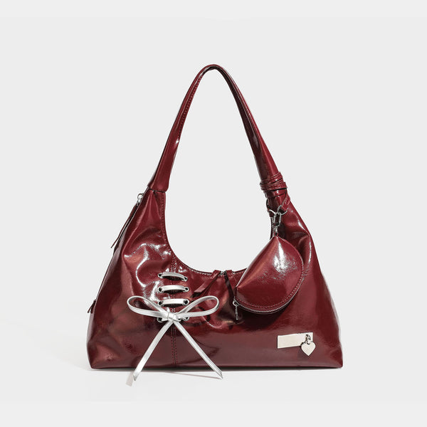 Weich fallende Hobo-Schultertasche mit glänzender Oberfläche in Lederoptik, silberfarbenen Schnürringösen und Schleife aus Ripsband auf der Vorderseite, Detail