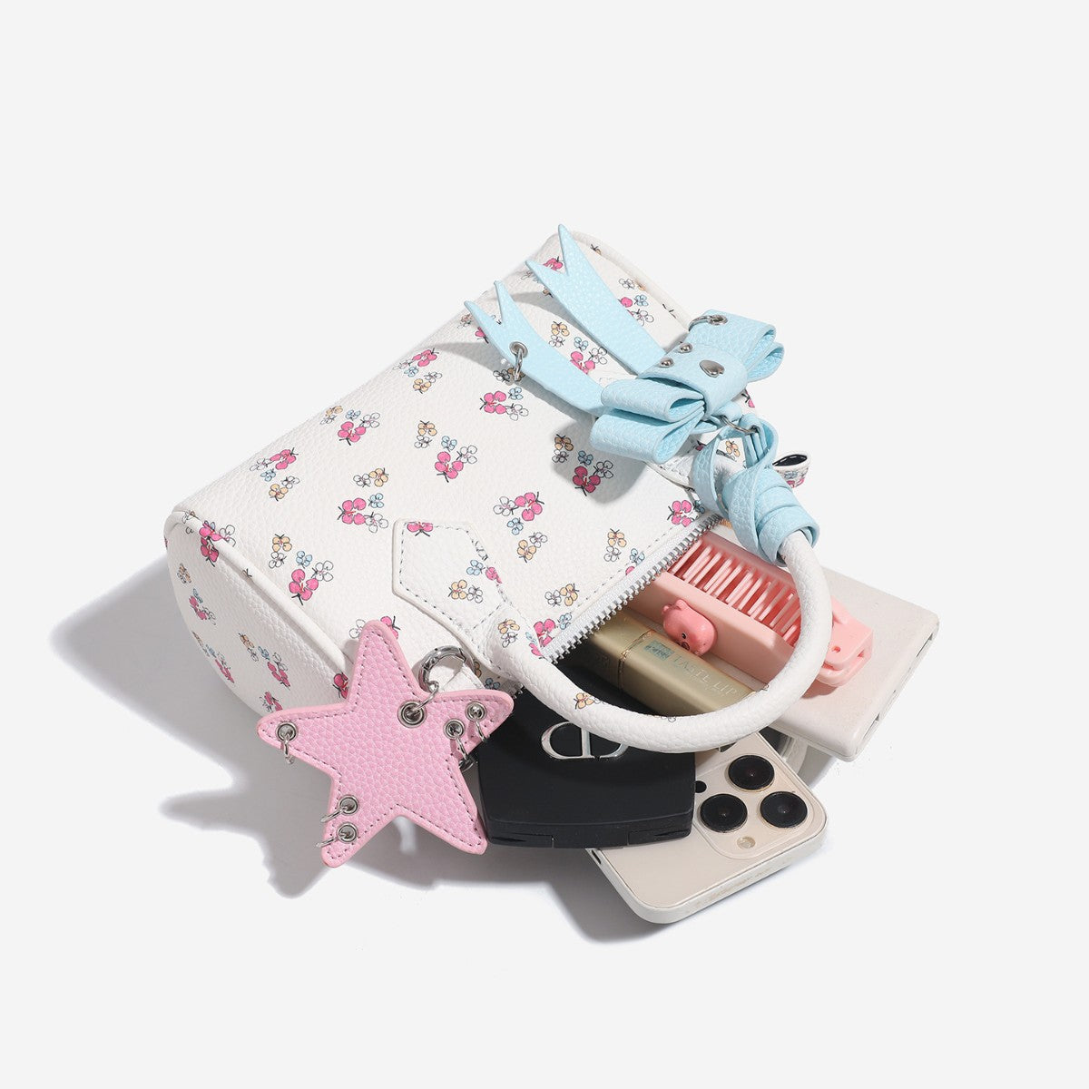 Weiße Mini-Boston-Handtasche mit genarbter Oberfläche und Blumen- oder Kirschprint, pastellblauem Schleifenanhänger, rosafarbenem Sternanhänger und zwei oberen Henkeln