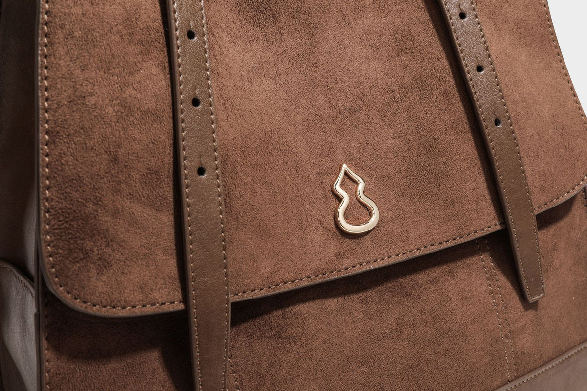 Structured suede-look convertible backpack handbag with flap closure and gold-tone emblem hardware in chocolate brown, detail