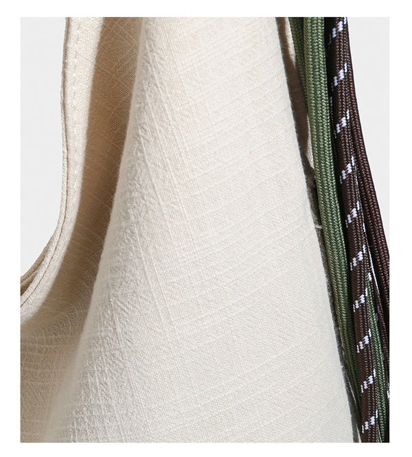 Soft slouchy cream canvas shoulder tote with braided brown and green cord handle, gold-tone ring hardware, and tassel trim