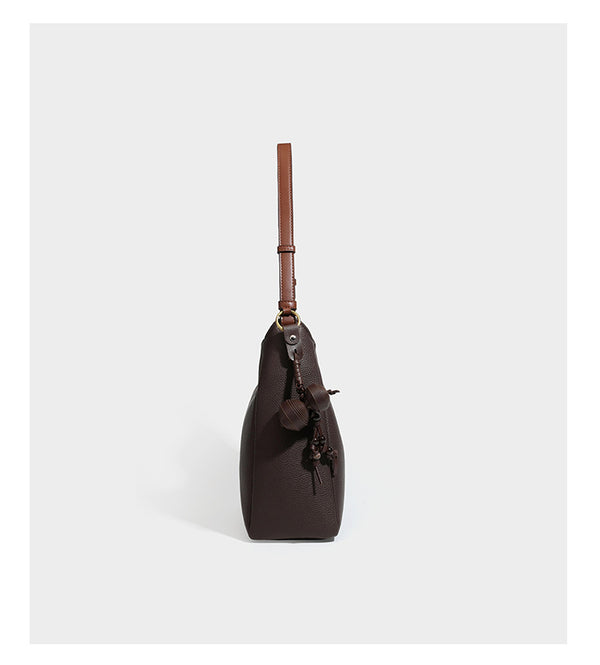 Hobo-Schultertasche in dunklem Espresso mit genarbter Oberfläche, warmen cognacfarbenen Details, verstellbarem schmalem Riemen, goldfarbenen Ringbeschlägen und geknotetem