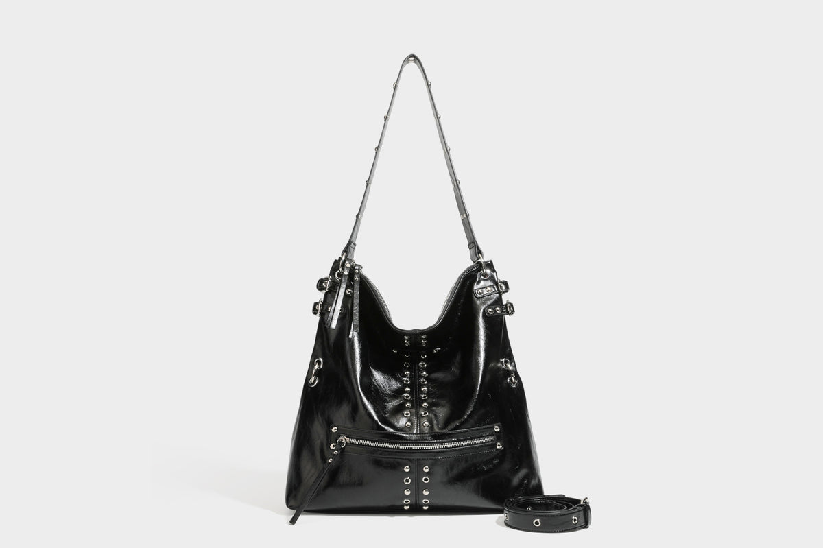 Black glossy leather-look slouchy shoulder bag with silver stud and eyelet hardware, top zip closure, front zip pocket, and