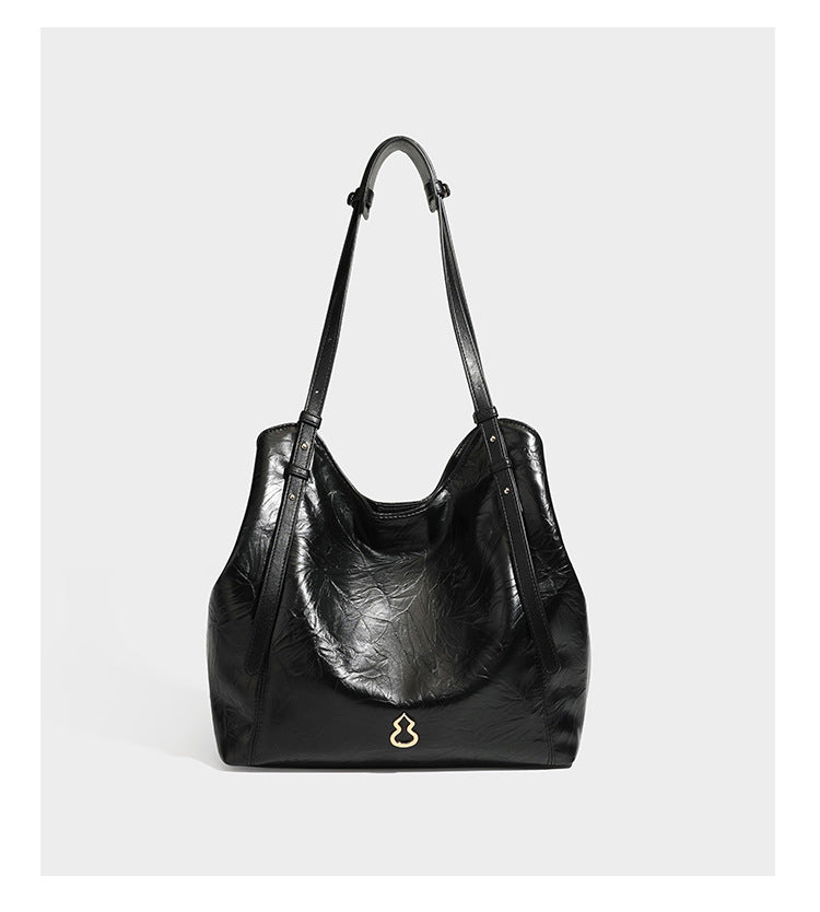 Große, glänzende Tote-Bag aus schwarzem Lederimitat mit geknitterter Optik, lässig fallender Trapezsilhouette, zwei Schulterriemen und goldfarbenen