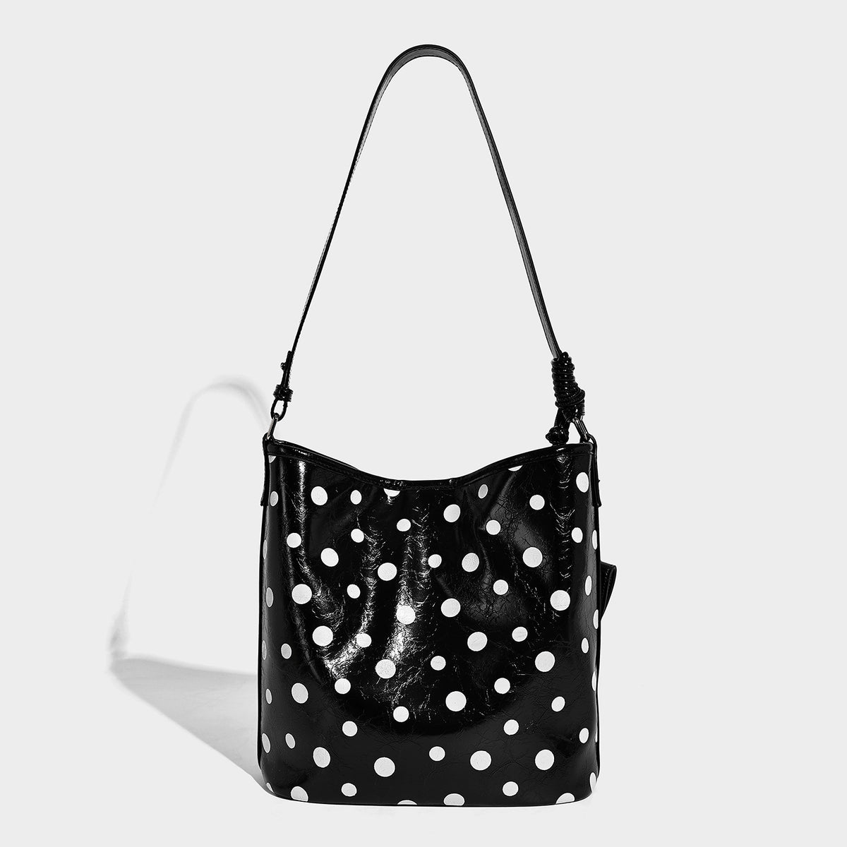 Glänzende schwarze Schultertasche im Bucket-Stil mit weißen Tupfen, langem verstellbarem Riemen und Kordelzugverschluss, Detailansicht 3