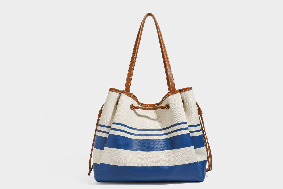 Large cream and navy striped canvas bucket tote bag with tan leather-look trim, drawstring closure, and double shoulder