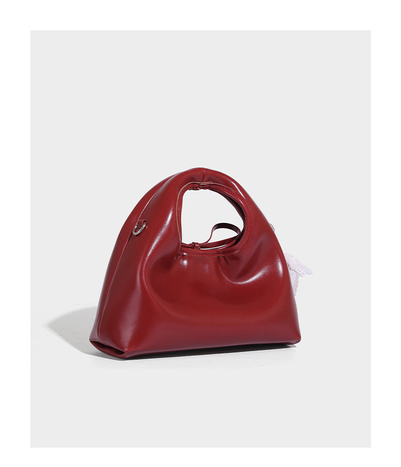 Kleine kuppelförmige Henkeltasche in glänzender Lederoptik mit Kordelzugverschluss, weißem Spitzen-Schleifenanhänger und silberfarbenen Metallbeschlägen