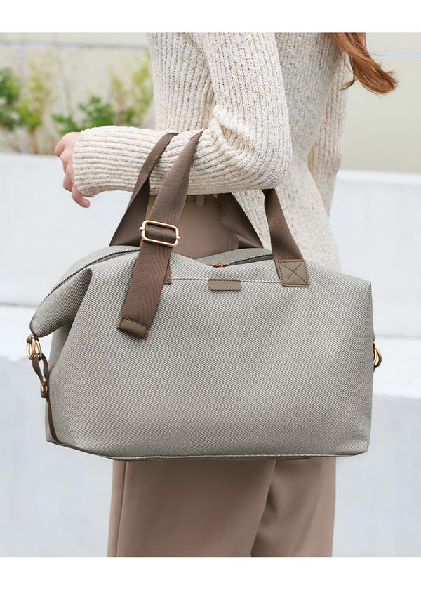 Structured woven duffel bag with dual tan webbing handles, detachable shoulder strap, top zip closure, and gold-tone
