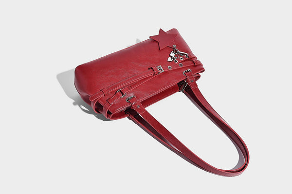 Structured glossy leather-look shoulder bag with wraparound belt straps, silver-tone hardware, and dangling star charm