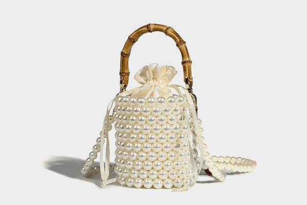 Small cylindrical bucket bag with glossy faux-pearl bead exterior, bamboo arched top handle, satin drawstring closure, and