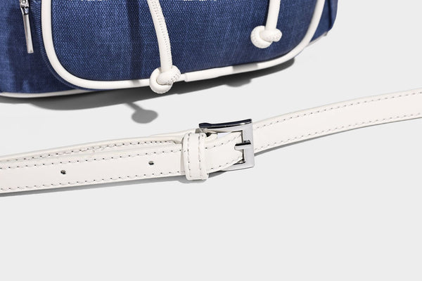 Compact denim drawstring backpack with white leather-look piping, flap-top buckle closure, front zip pocket, and silver-tone