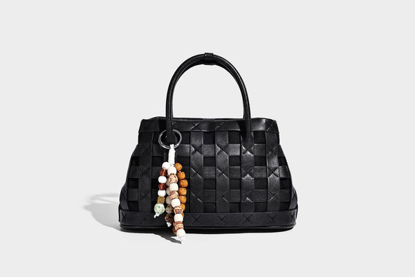 Small structured woven satchel tote with rounded top handles, silver-tone ring hardware, and bead tassel charm, detail view