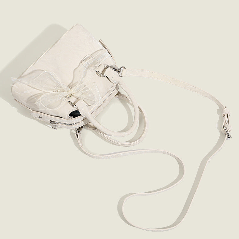 Small structured Boston bag in cream with glossy crinkled finish, sheer bow accent, silver-tone hardware, dual top handles