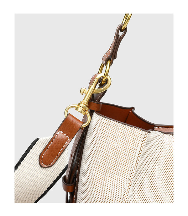 Cream canvas and tan leather-look bucket bag with arched top handle, wide detachable shoulder strap, and gold-tone hardware