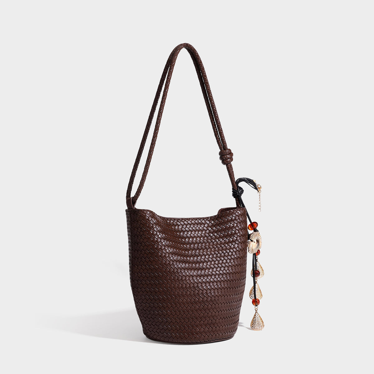 Olive green woven leather-look bucket bag with braided crossbody strap, knotted adjustment, and gold-tone tassel charm with