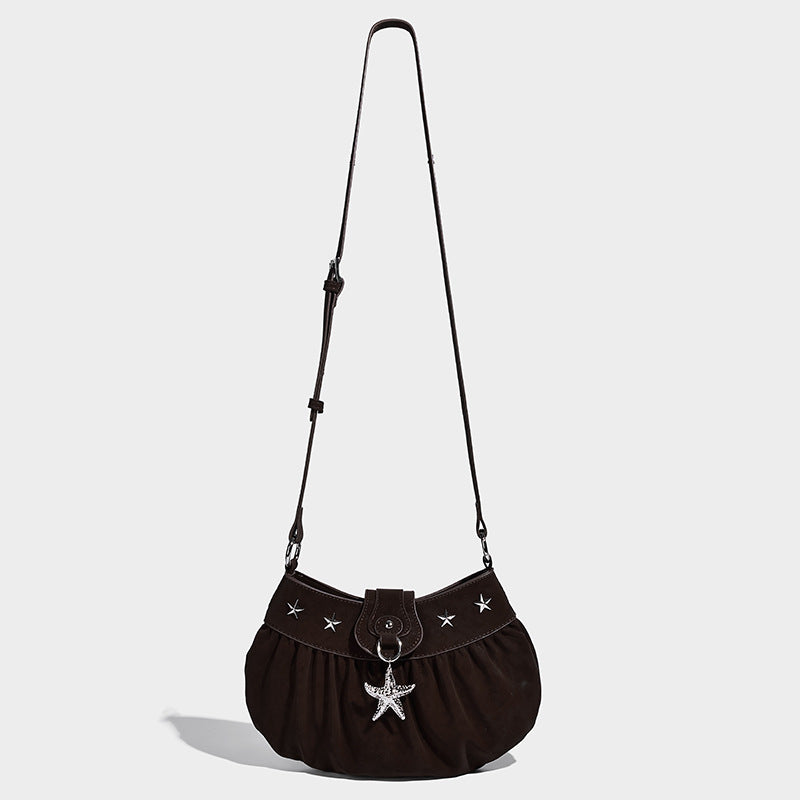 Ruched shoulder bag with curved flap, silver star studs, dangling starfish charm, and adjustable crossbody strap, detail view