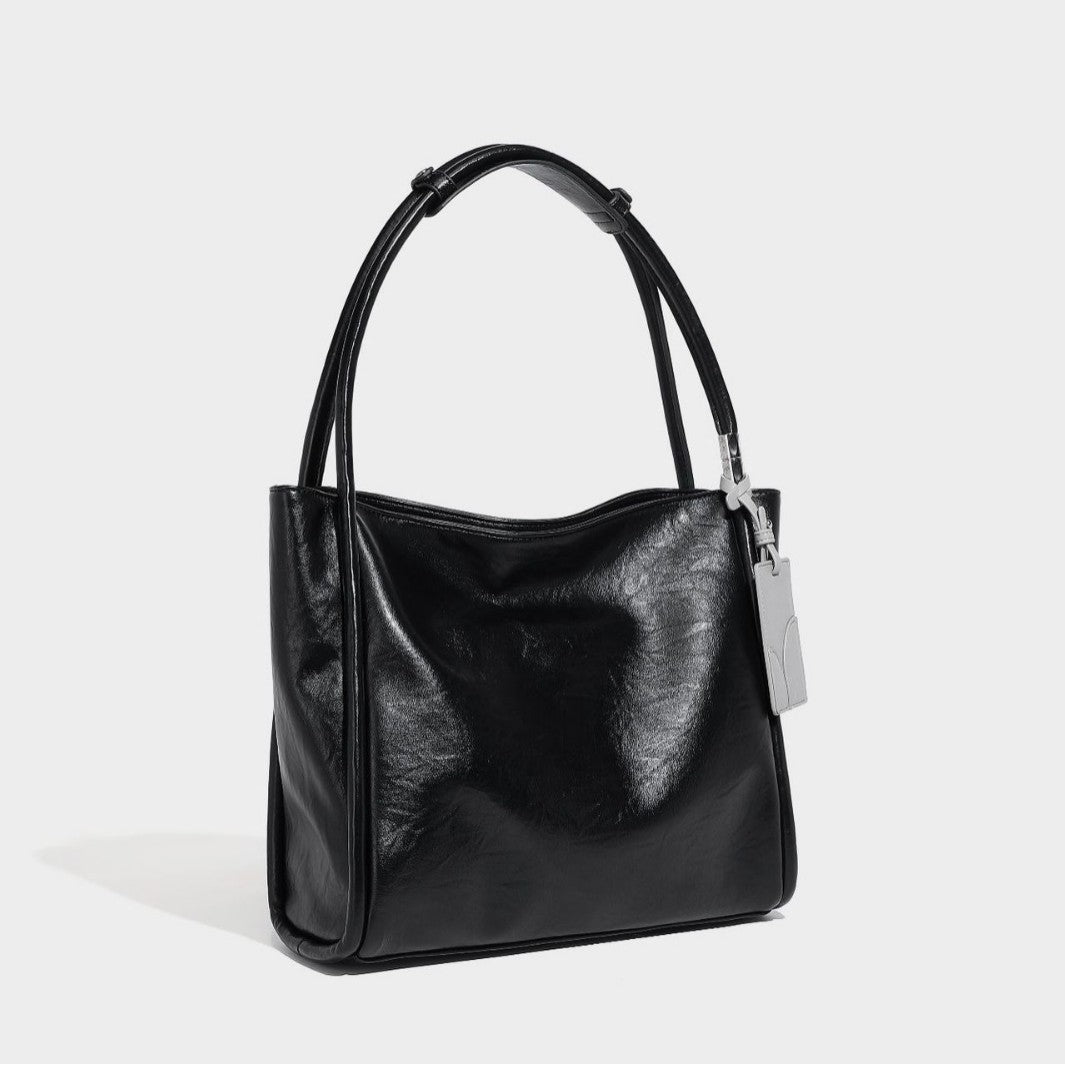 Black glossy leather-look tote bag with twin round top handles and silver-tone hardware, front view