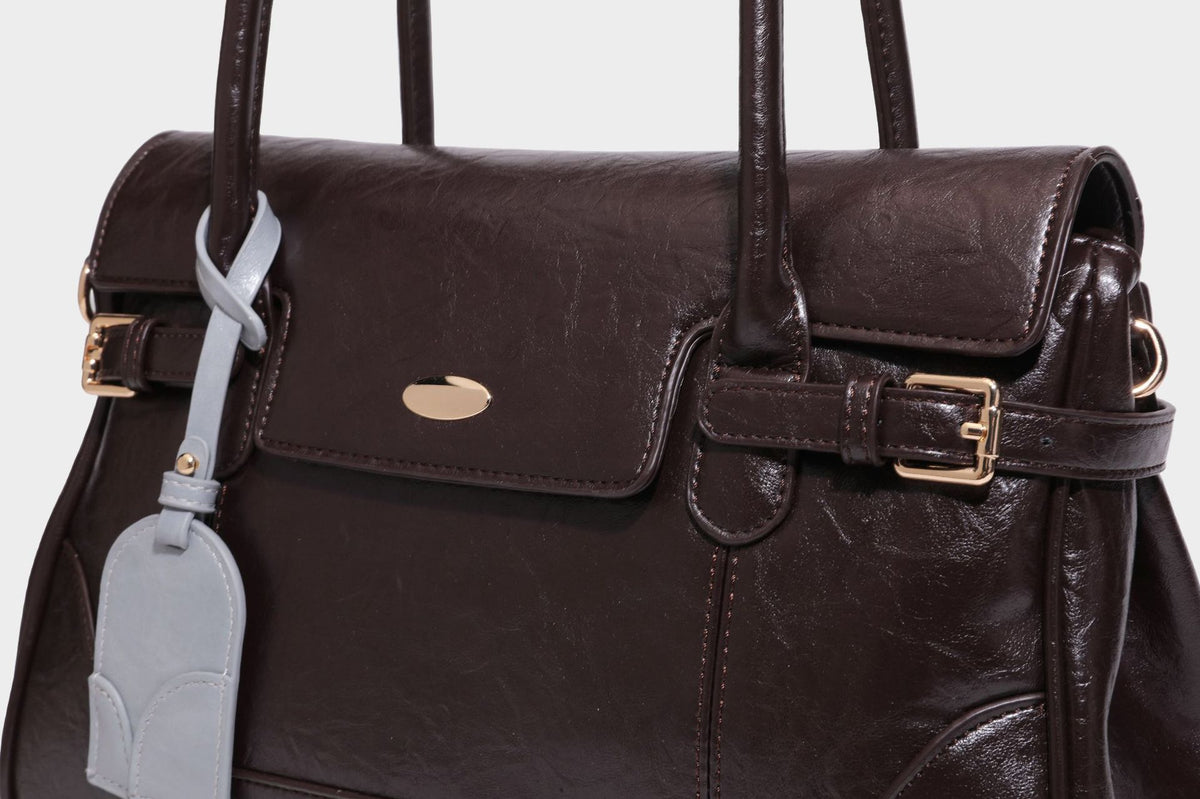 Structured glossy leather-look satchel bag with flap closure, gold-tone buckle accents, double top handles, detachable