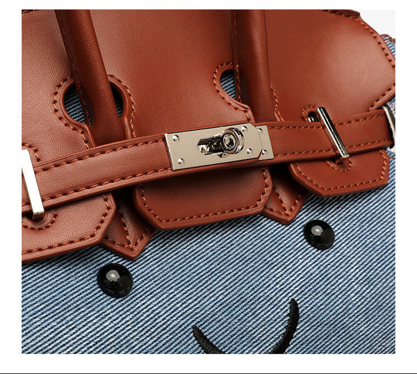 Small structured trapezoid satchel bag with smiling face motif, pom-pom accents, brown leather-look trim, silver-tone, detail