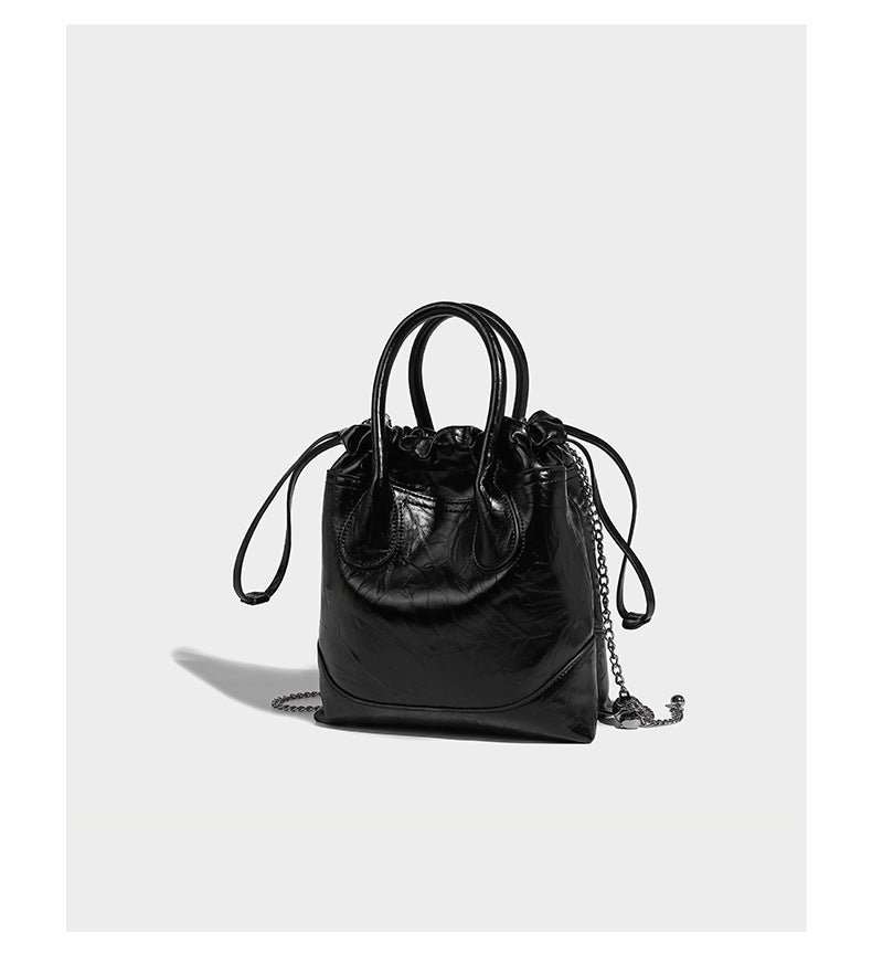 Glossy crinkled ruched drawstring bucket bag with rounded double top handles and detachable chain crossbody strap, detail