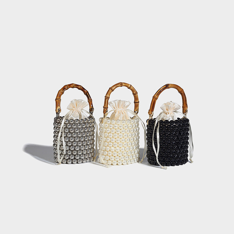 Small cylindrical bucket bag with glossy faux-pearl bead exterior, bamboo arched top handle, satin drawstring closure, and