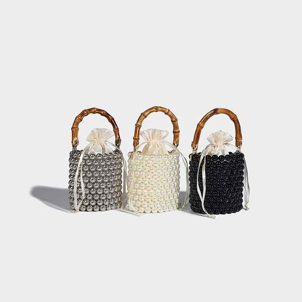 Small cylindrical bucket bag with glossy faux-pearl bead exterior, bamboo arched top handle, satin drawstring closure, and