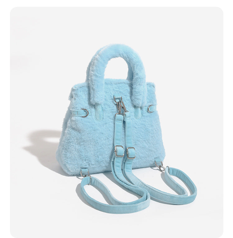 Ice-blue plush faux-fur Kelly-style convertible bag with embroidered smiling face, dark pom-pom feet, silver-tone clasp
