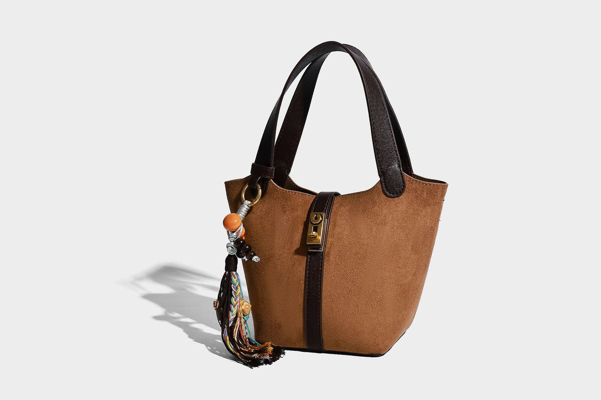 Small structured trapezoid tote bag in matte suede-look finish with black contrast trim, gold-tone front clasp, tassel charm