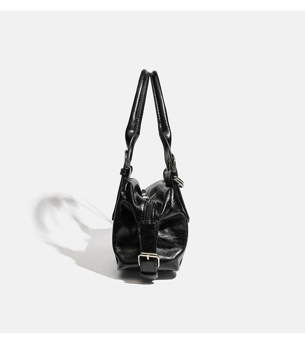 Compact black glossy leather-look satchel bag with silver-tone rivets, buckle hardware, and dual padded top handles, detail