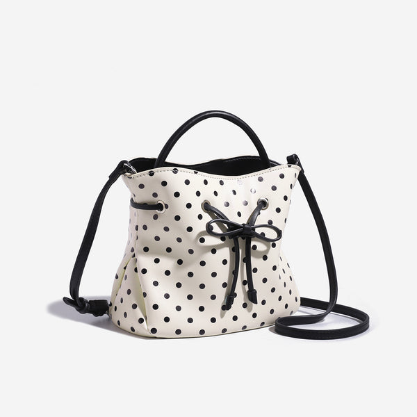 Cream white polka-dot drawstring bucket bag with black leather-look top handle and bow-tied cord closure, detail view 3