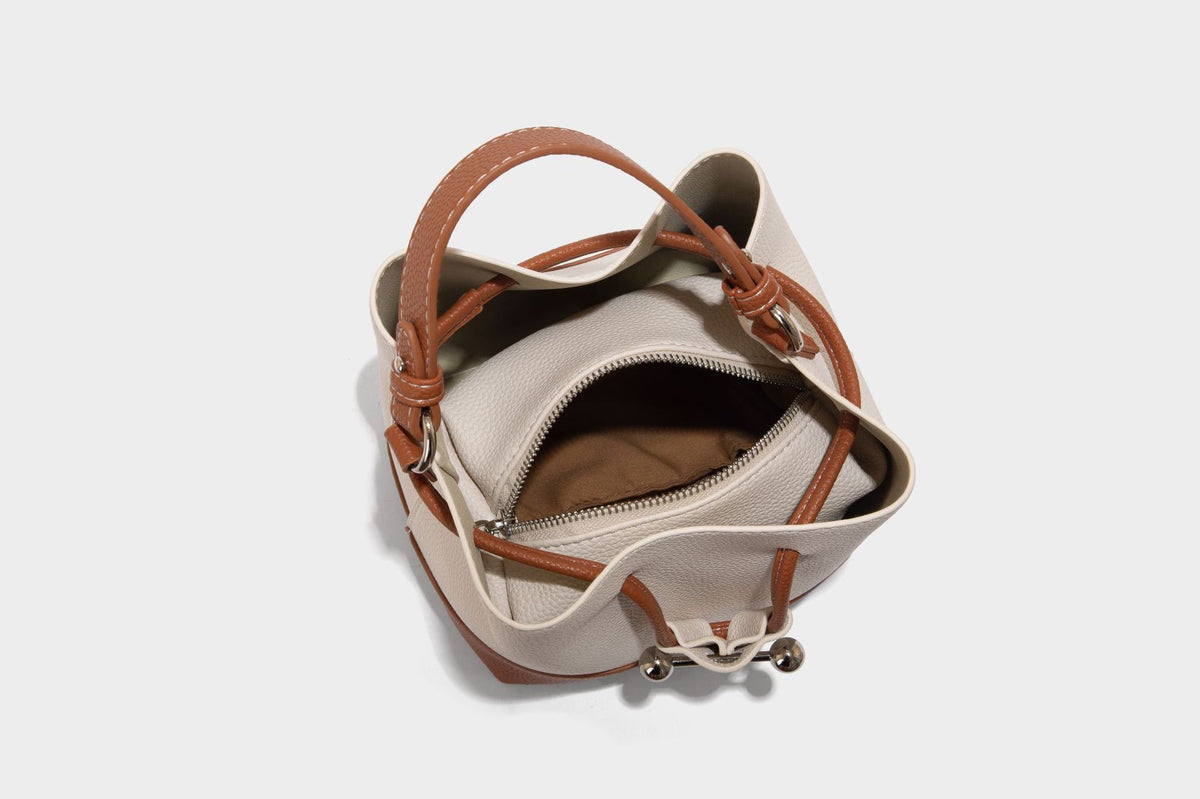 Small two-tone pebbled drawstring bucket bag with tan contrast base, metal toggle hardware, short top handle, and detachable