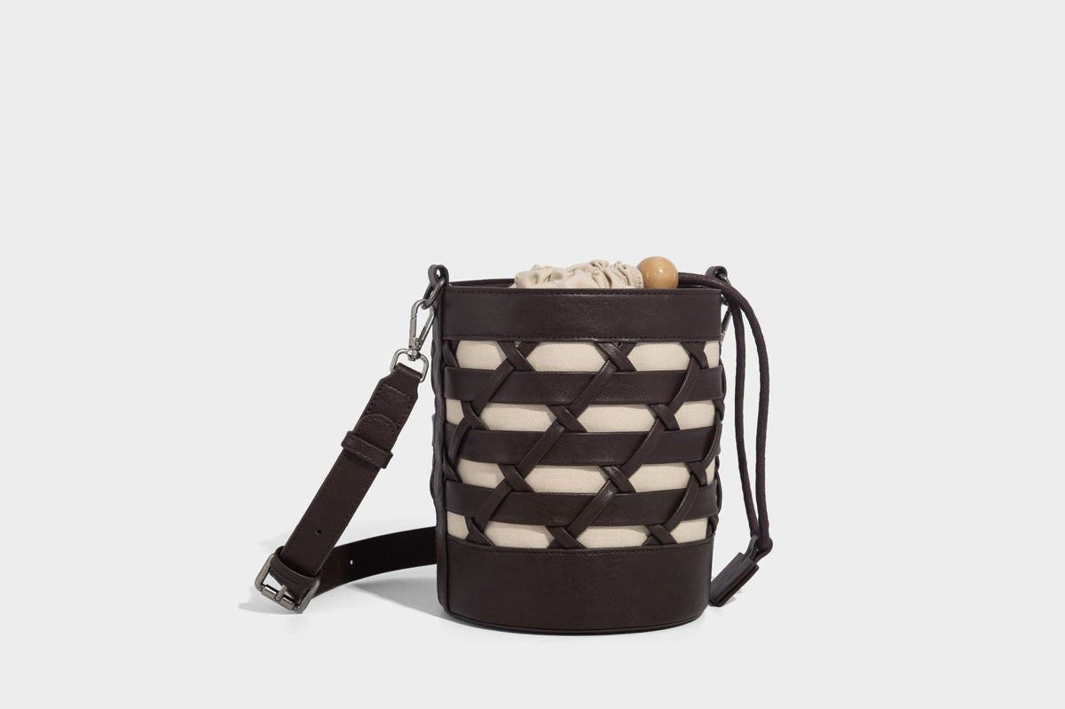 Small cylindrical woven lattice bucket bag with leather-look black trim, beige canvas body, wooden bead drawstring closure