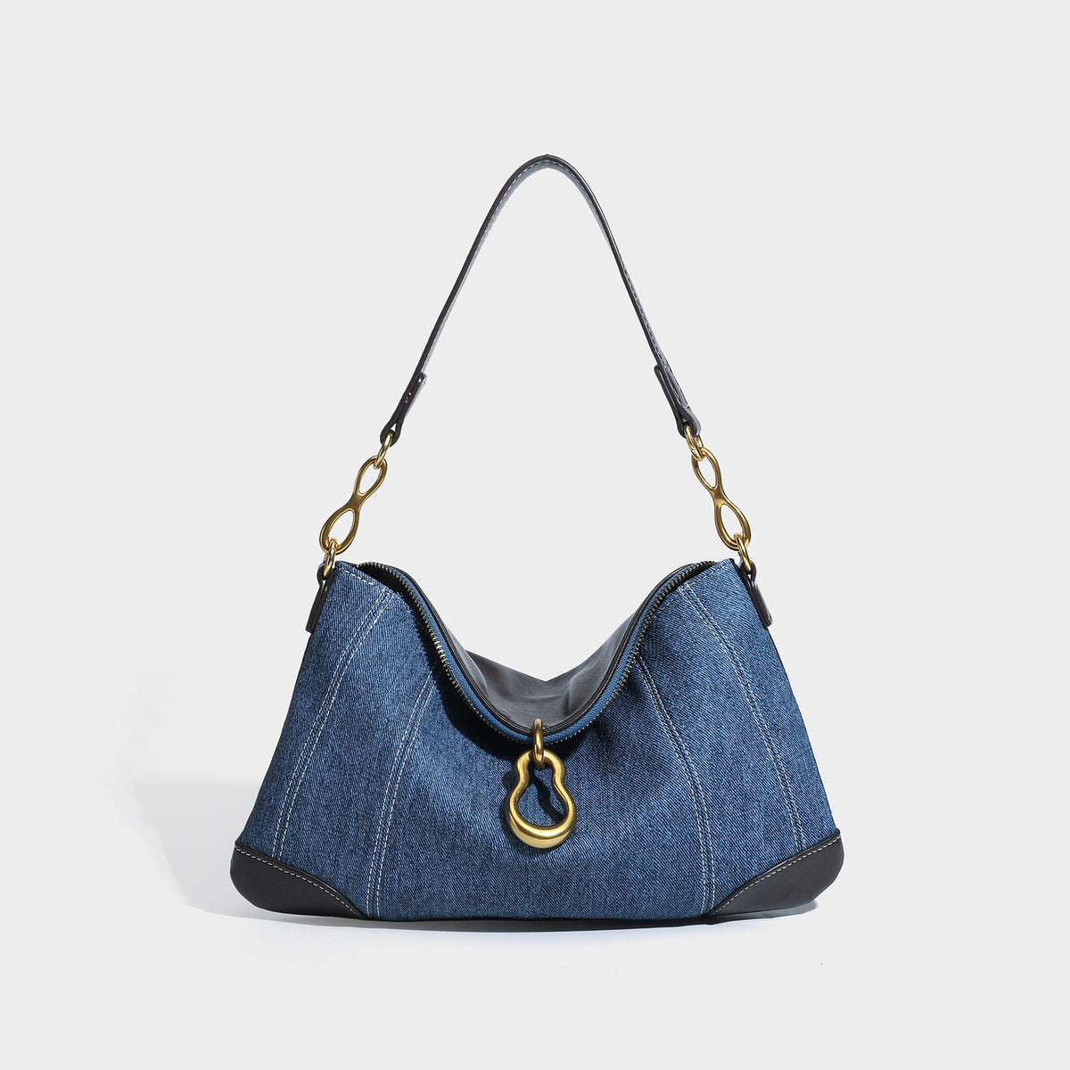 Slouchy denim shoulder bag with dark leather-look trim, gold-tone chain-link hardware, and top zipper closure, front view