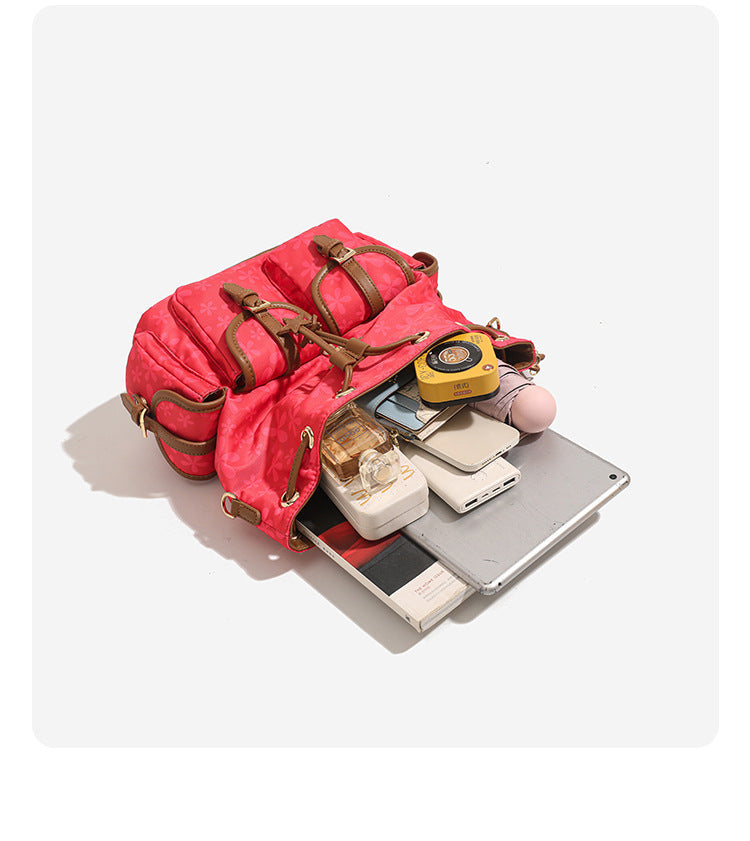 Red floral-print backpack handbag with brown leather-look trim, dual front buckle pockets, star charms, and gold-tone, detail