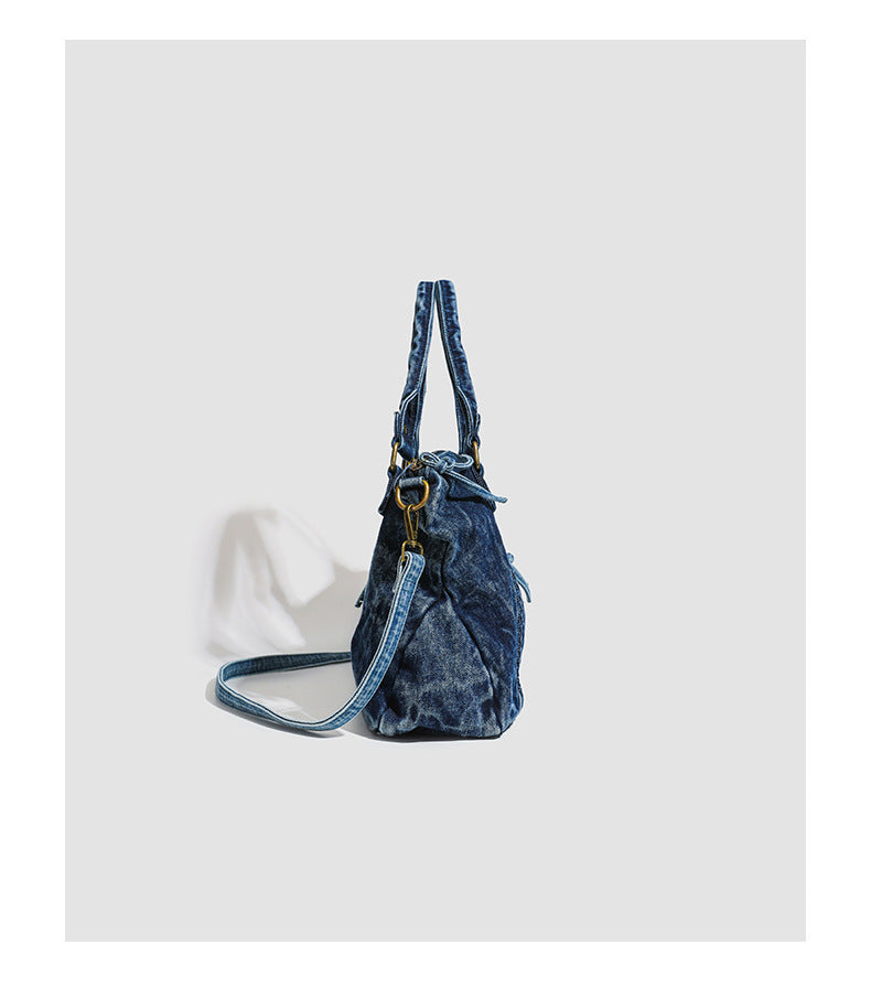 Large washed blue denim-look shoulder bag with gold-tone rings and rivets, top zip closure, front zip pocket, and adjustable