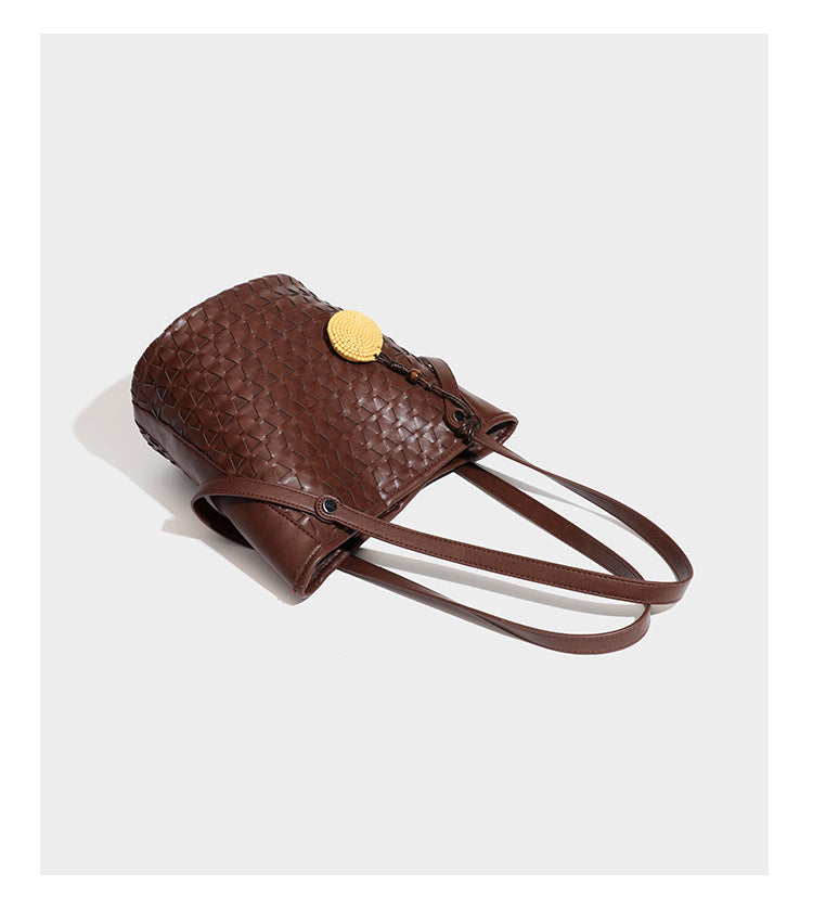 Brown embossed geometric woven leather-look bucket tote bag with dual shoulder straps, side snap hardware, and a round