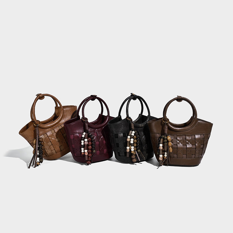 Small woven-panel bucket bag with circular ring handles, beaded tassel charm, and detachable crossbody strap in brown, detail