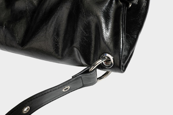 Black glossy leather-look slouchy shoulder bag with silver stud and eyelet hardware, top zip closure, front zip pocket, and