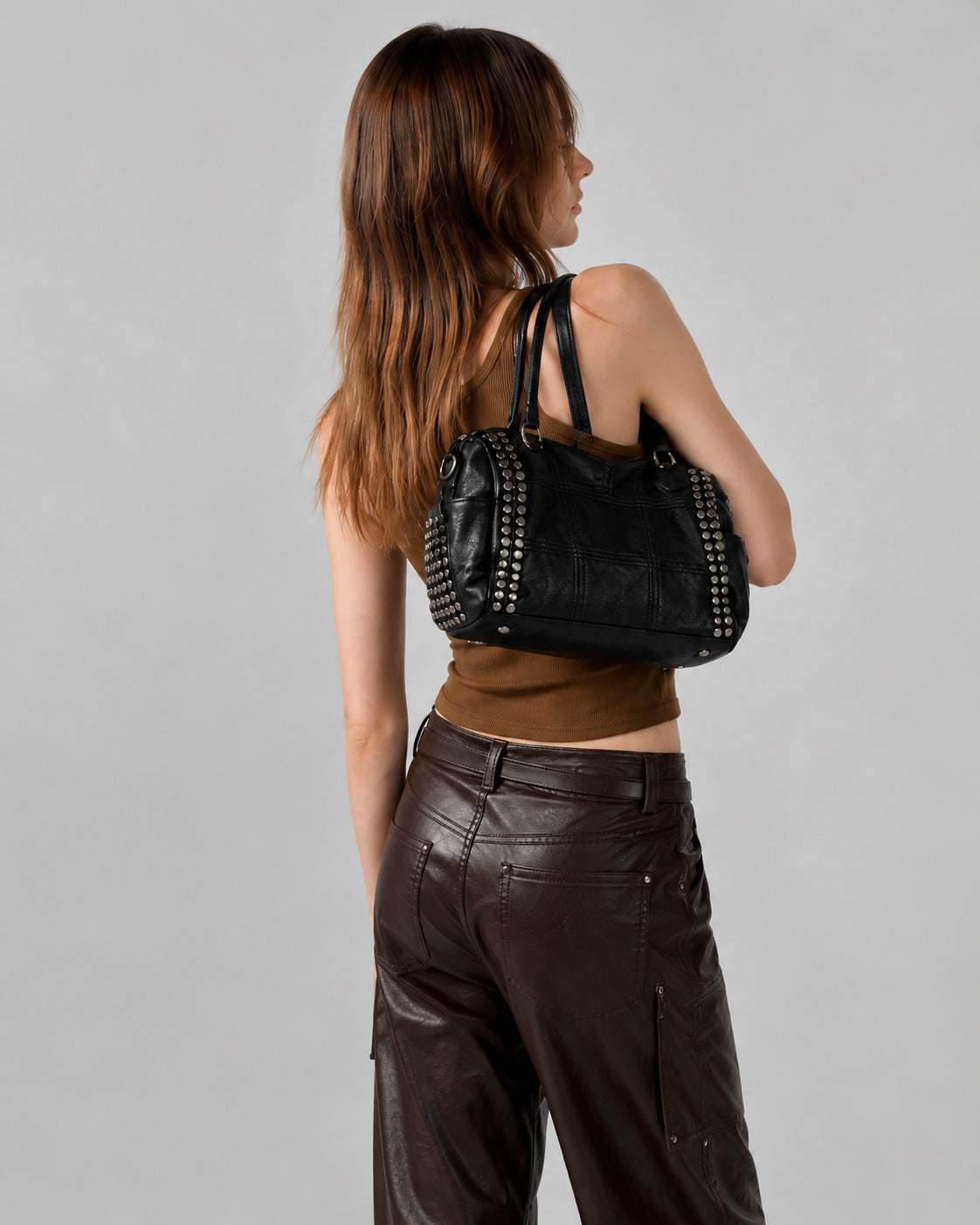 Black leather-look satchel bag with gunmetal rivet trim, grid-stitched paneling, dual rolled top handles, and curved zip