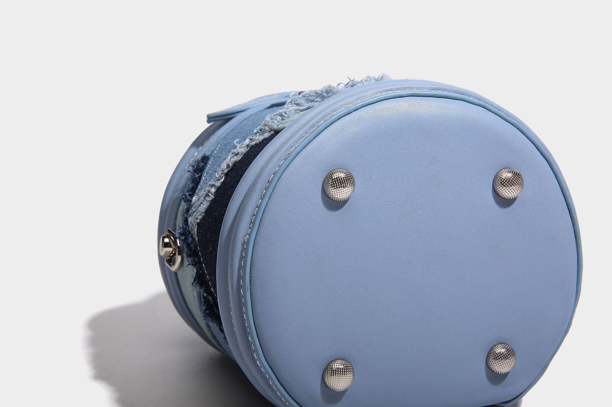 Mini cylindrical barrel bucket bag in denim patchwork with frayed edges, smooth leather-look trim, zip-around top closure