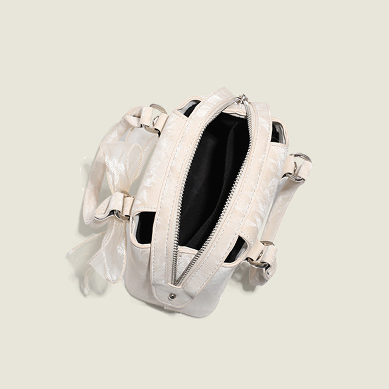Small structured Boston bag in cream with glossy crinkled finish, sheer bow accent, silver-tone hardware, dual top handles