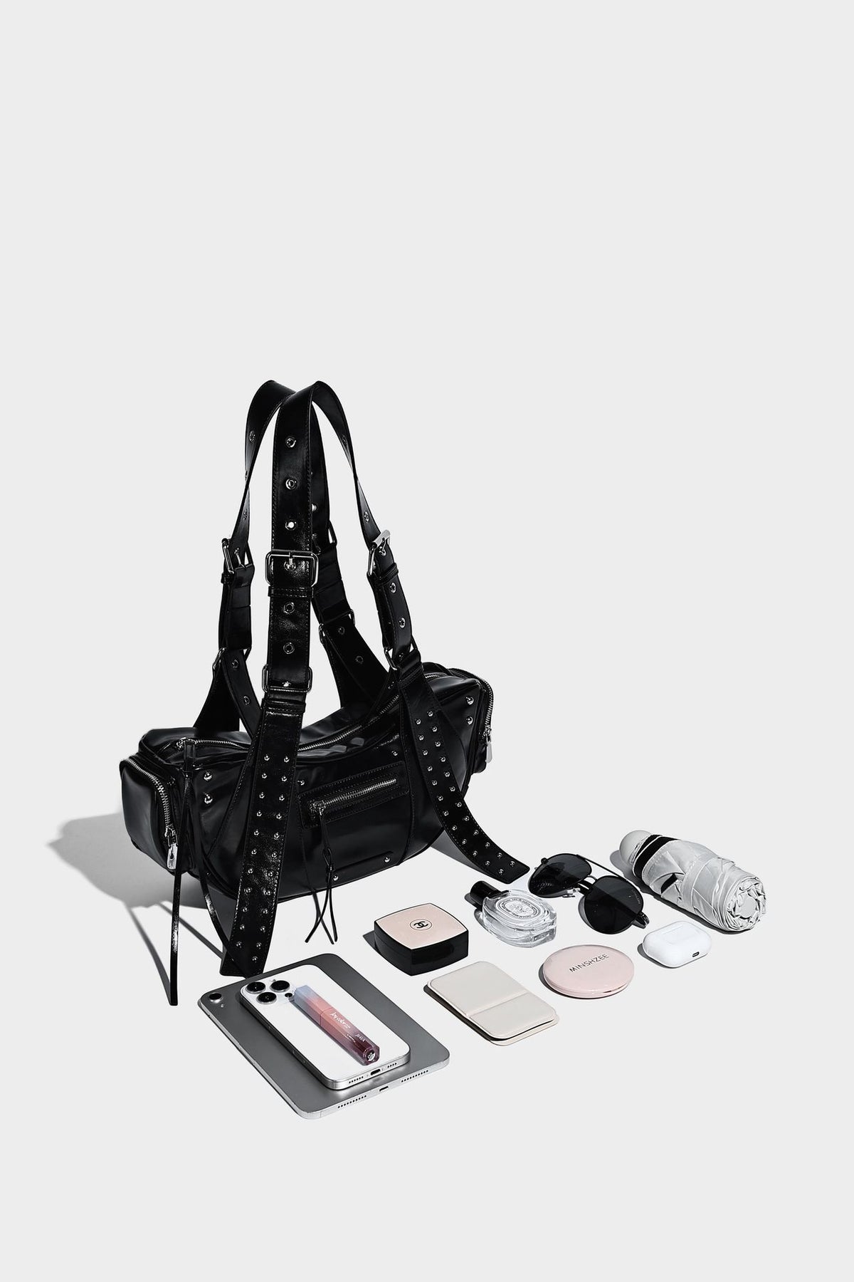 Glossy black crescent shoulder bag with silver-tone rivets, multiple zip pockets, and long adjustable studded straps, detail