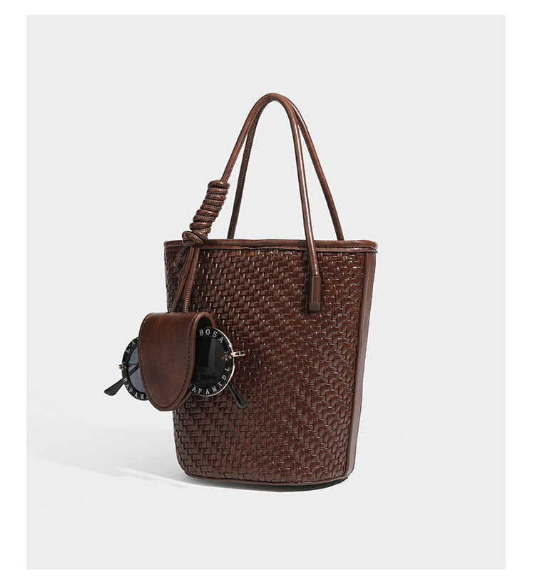 Structured woven-texture leather-look bucket bag in brown with knotted top handles, small front flap pouch, and adjustable