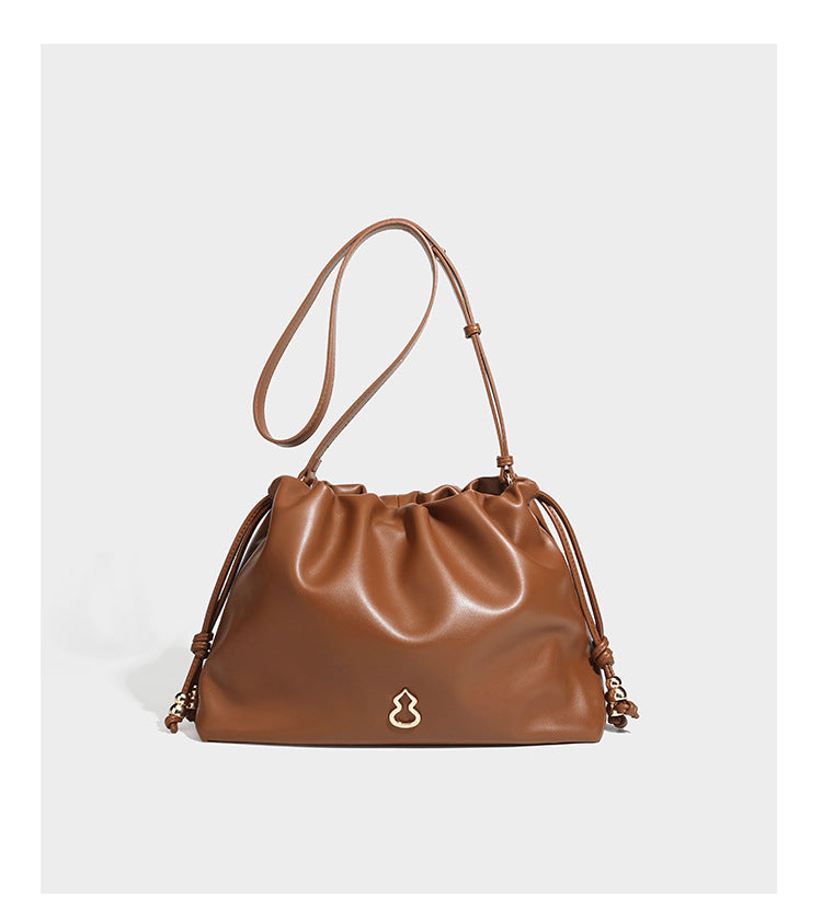Slouchy ruched drawstring shoulder bag in smooth leather-look finish with gold-tone emblem and slim adjustable strap, detail