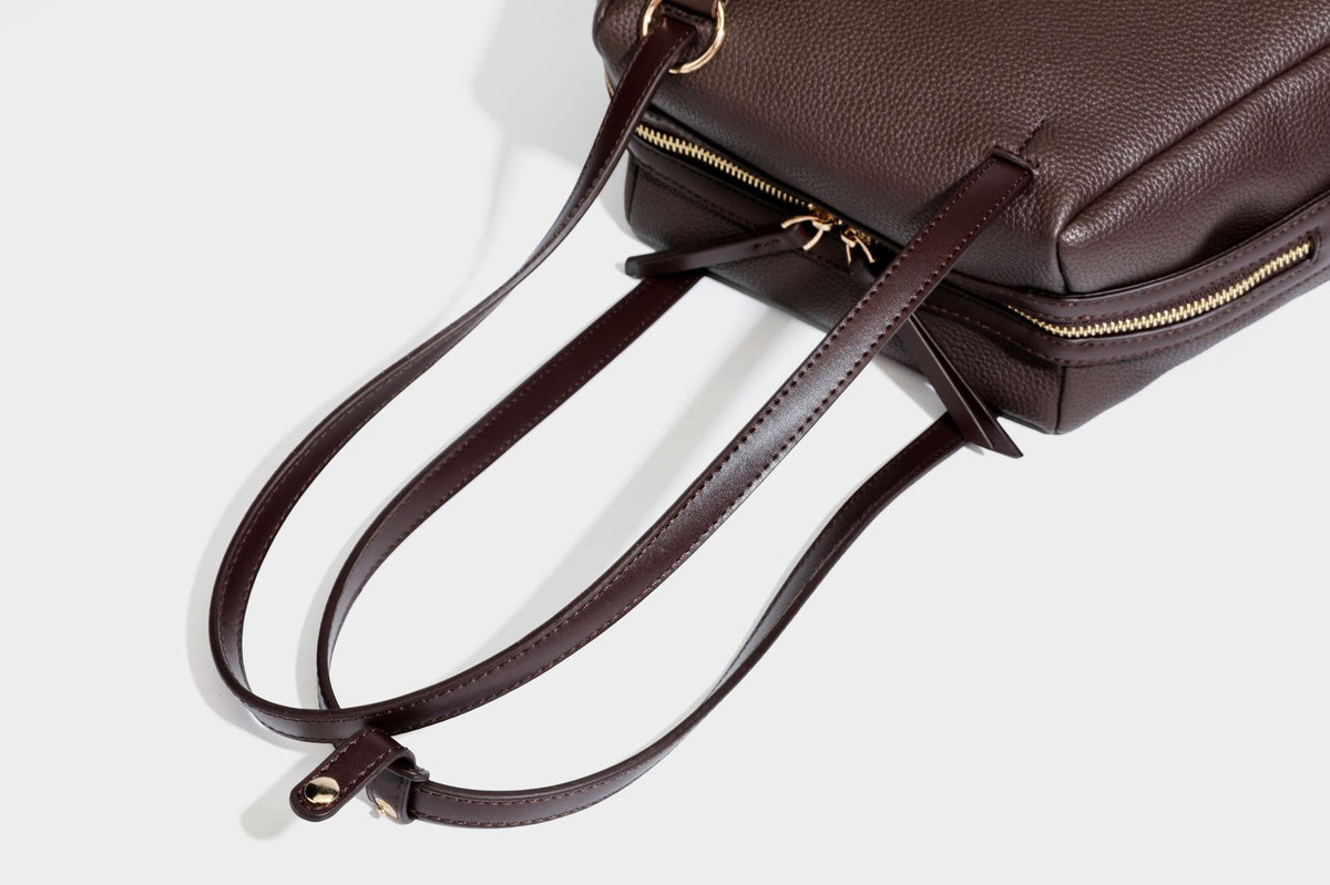 Structured trapezoid shoulder bag in dark brown pebbled leather-look finish with slim double straps, top zip closure, side