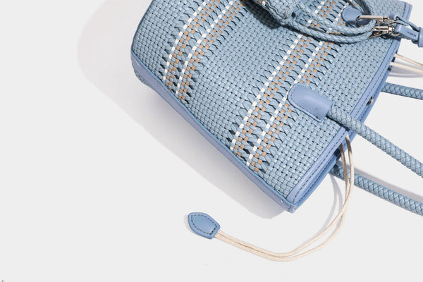 Light blue open-weave woven bucket tote bag with long braided shoulder straps, drawstring side ties, and attached mini pouch