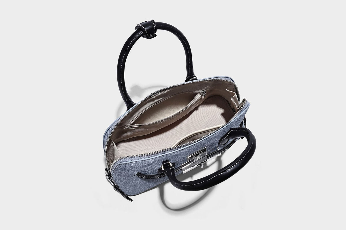 Compact structured satchel in light blue denim-look fabric with black leather-look trim, silver turn-lock closure, rolled
